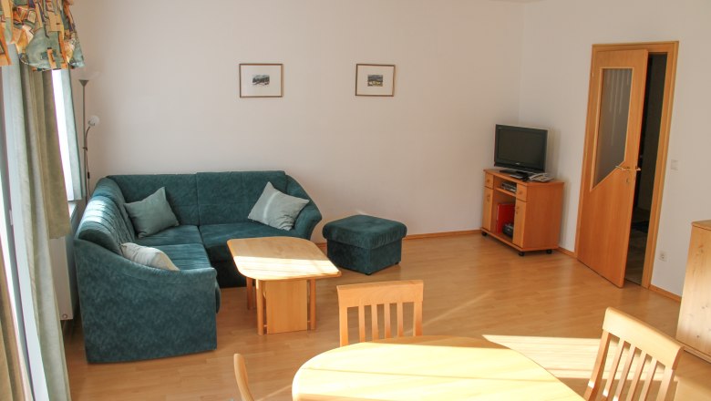 Apartment 70m², © Haus Lenz Living room with green corner sofa, wooden table, TV and dining table.