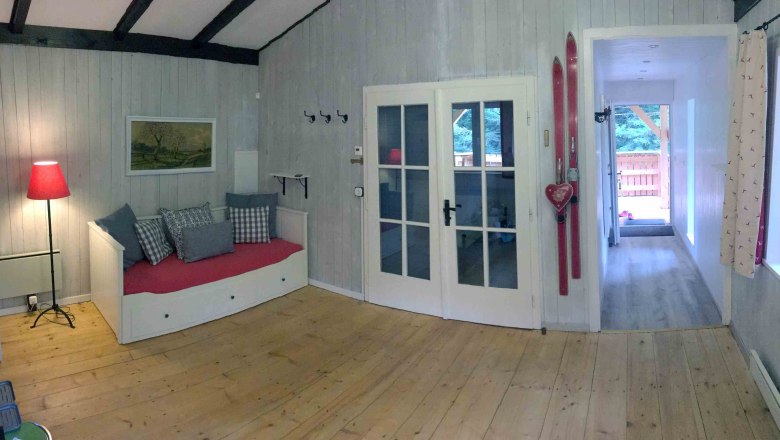 Vacation home, © Marianne Gschaider Interior view of a cozy vacation home with wooden floor, red sofa, skis on the wall and glass doors.