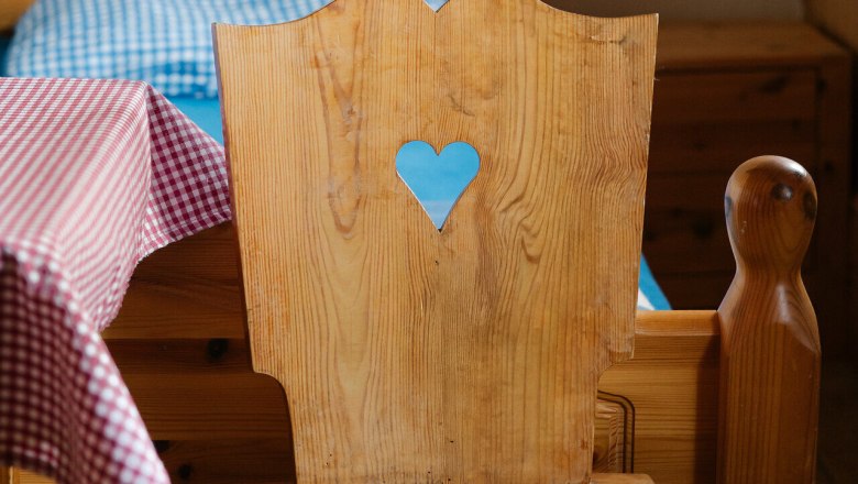 Edelweiß Hut, Schneeberg, hut, Schneebergland, Vienna Alps in Lower Austria, © Wiener Alpen/Sophie Menegaldo A rustic wooden chair with a heart-shaped cutout in front of a bed at the Edelweißhütte on Schneeberg