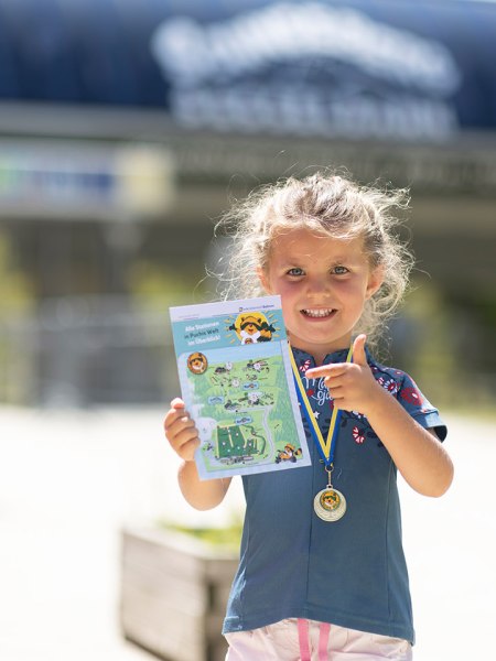 Kleines Mädchen zeigt stolz seinen fertig abgestempelten Stempelpass und trägt auch schon die überreichte Medaille.