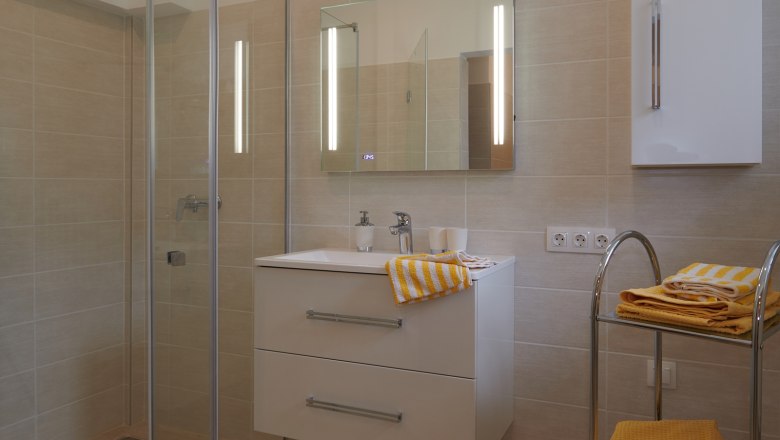 Bathroom, © Landhaus Puchbergerhof by smc Modern bathroom with shower, washbasin and yellow towels.