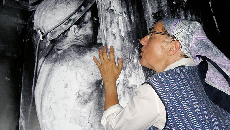 Mrs. Franzi, © Andrea Zach A woman with a headscarf looks at a large black and white photo of a miner.
