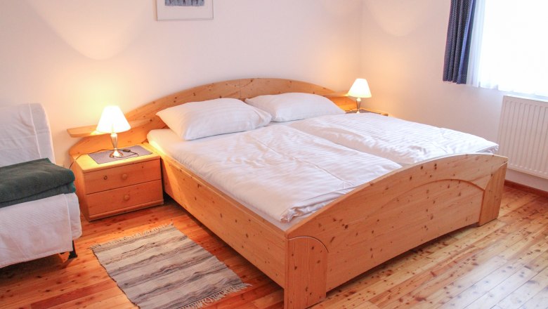 Wohnung 70m², © Haus Lenz Gemütliches Schlafzimmer mit Doppelbett, Holzboden und Nachttischen mit Lampen.