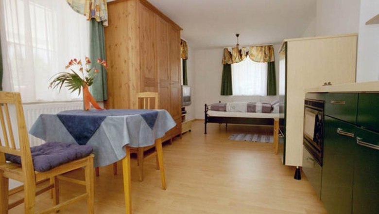 Apartment 30m², © Haus Lenz Small apartment with wooden furniture, dining table, chairs, bed and kitchenette.