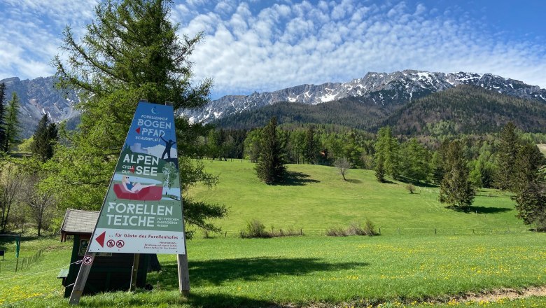 Relaxation and adventure around the Forellenhof, © Wiener Alpen Sign in front of a mountain landscape with meadow and trees.