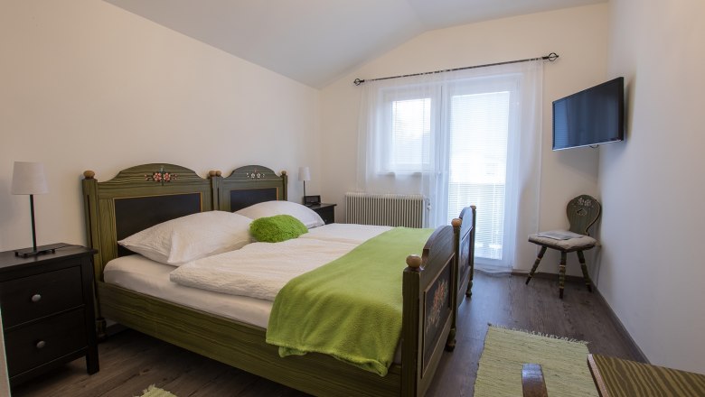 Common room, © Dirnbauer Cozy bedroom with double bed, green comforter and TV on the wall.