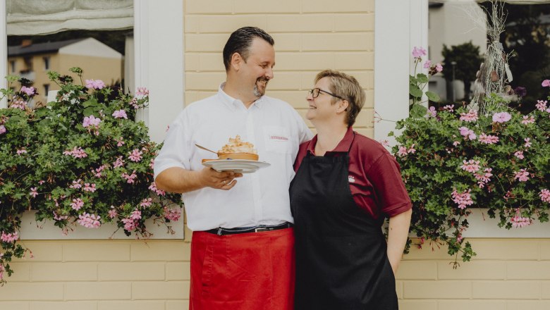 Hosts: Elisabeth and Thomas Jautschnig, © Niederösterreich Werbung/Rita Newman A man and a woman stand smiling in front of a window with flowers.