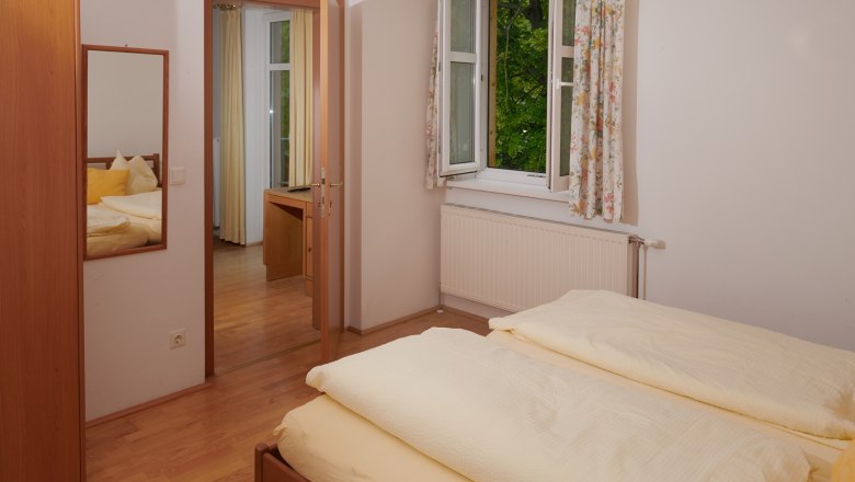 Bedroom, © Landhaus Puchbergerhof by smc A bedroom with a double bed, an open window with curtains and a mirror on the wall.