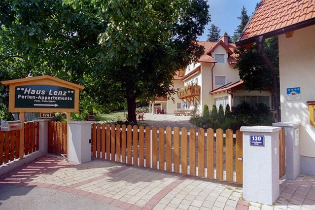 House Lenz, © Haus Lenz Entrance to Haus Lenz with wooden fence and sign, surrounded by trees.