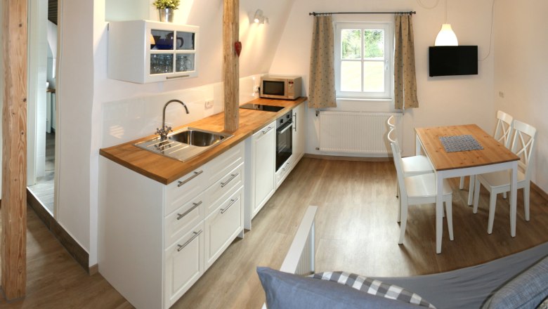 Apartment 1, © Marianne Gschaider Modern kitchen with wooden floor, white cupboards, dining table and window.