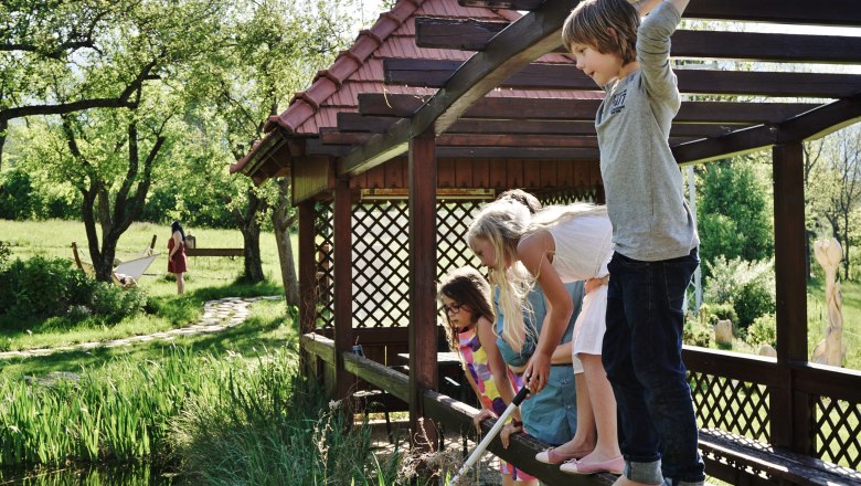 Biotope, © Gasthof Schmirl Children playing on a wooden bridge over a pond in a garden.