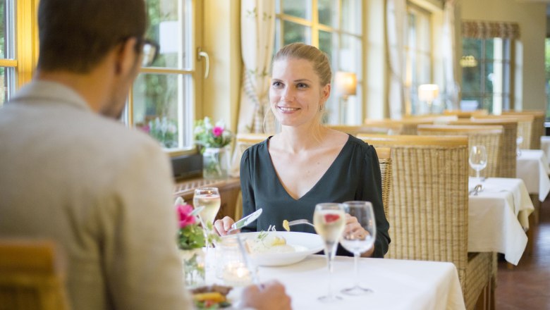 Alpen-Aktiv Country Inn "Zur Schubertlinde", © Patrick Haberler A couple having dinner in a cozy restaurant with large windows and candlelight.