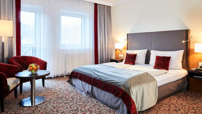 Doppelzimmer Hotel Schneeberghof, © Hotel Schneeberghof Doppelzimmer im Hotel Schneeberghof mit Doppelbett, roten Kissen, Tisch mit Obstschale und zwei Sesseln.