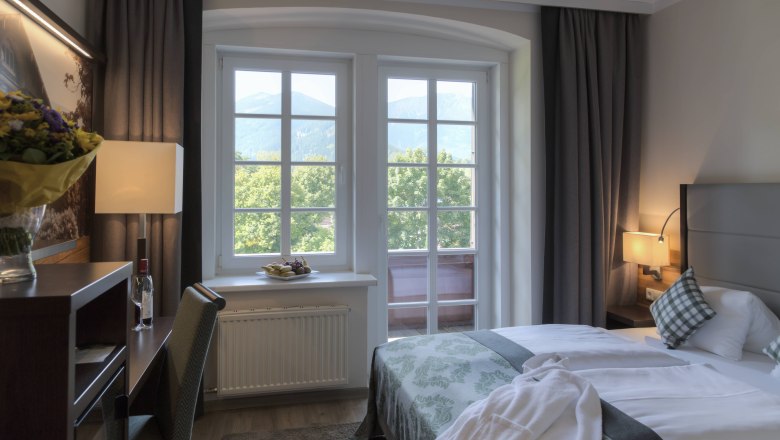 Ein gem&uuml;tliches Hotelzimmer mit Doppelbett, Fenster mit Bergblick, Schreibtisch und Blumen.