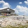 Fischerh&uuml;tte auf dem Schneeberg mit Wanderern und blauem Himmel.