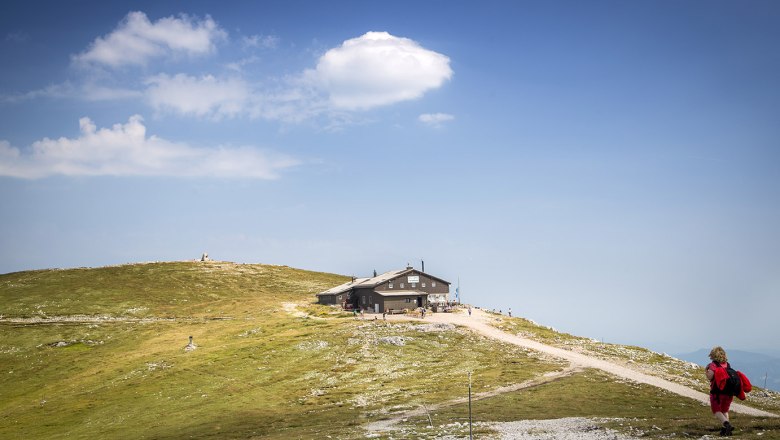 Eine Bergh&uuml;tte auf einem H&uuml;gel mit blauem Himmel und Wolken im Hintergrund.
