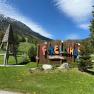 Eingang zum Forellino Kinderspielplatz mit Berglandschaft im Hintergrund.