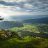 Blick von einer Felskante auf eine gr&uuml;ne Landschaft mit H&uuml;geln und einem Dorf im Tal.