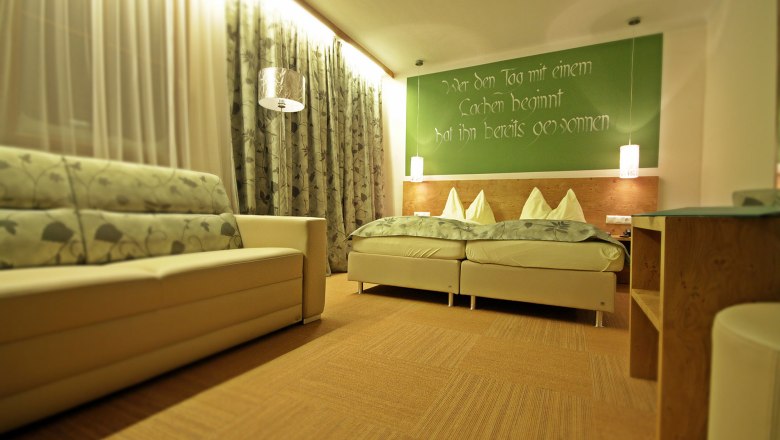 Gem&uuml;tliches G&auml;stezimmer mit Doppelbett, Sofa und dekorativen Vorh&auml;ngen.