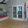Interior view of a cozy vacation home with wooden floor, red sofa, skis on the wall and glass doors.