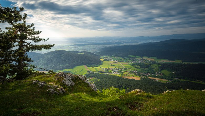 Blick von einer Felskante auf eine gr&uuml;ne Landschaft mit H&uuml;geln und einem Dorf im Tal.