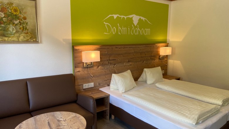 Gem&uuml;tliches Doppelzimmer mit Holzm&ouml;beln, Sofa, Tisch und Wanddekoration.