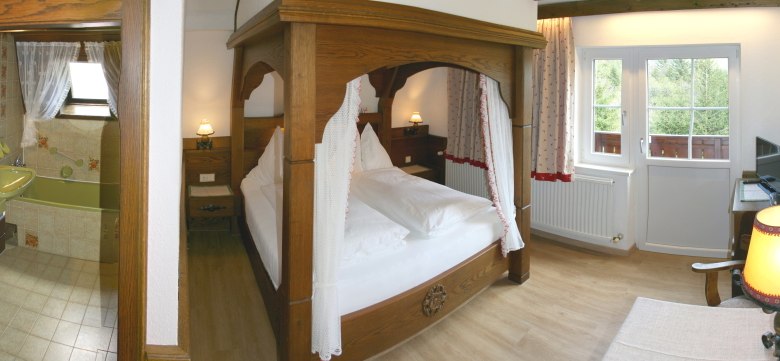 Gem&uuml;tliches Schlafzimmer mit Himmelbett, angrenzendem Badezimmer und Balkonzugang.