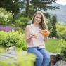 Frau sitzt im Garten und gie&szlig;t Saft in ein Glas.