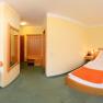 Panorama of a hotel room with double bed, table, two armchairs and TV.