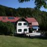 A traditional house with a red roof, surrounded by forest and meadow, with the inscription 'Gschaiderhof'.