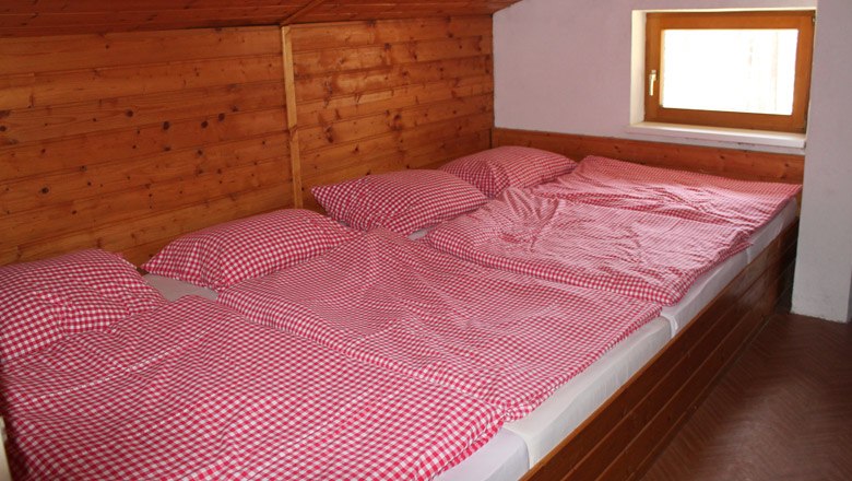 Drei Betten mit rot-wei&szlig; karierten Bettbez&uuml;gen in einem holzverkleideten Raum.
