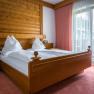 A cozy bedroom with a wooden double bed, white comforters and red curtains in front of a window.