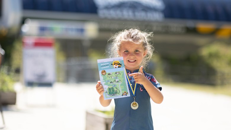 Kleines Mädchen zeigt stolz seinen fertig abgestempelten Stempelpass und trägt auch schon die überreichte Medaille.