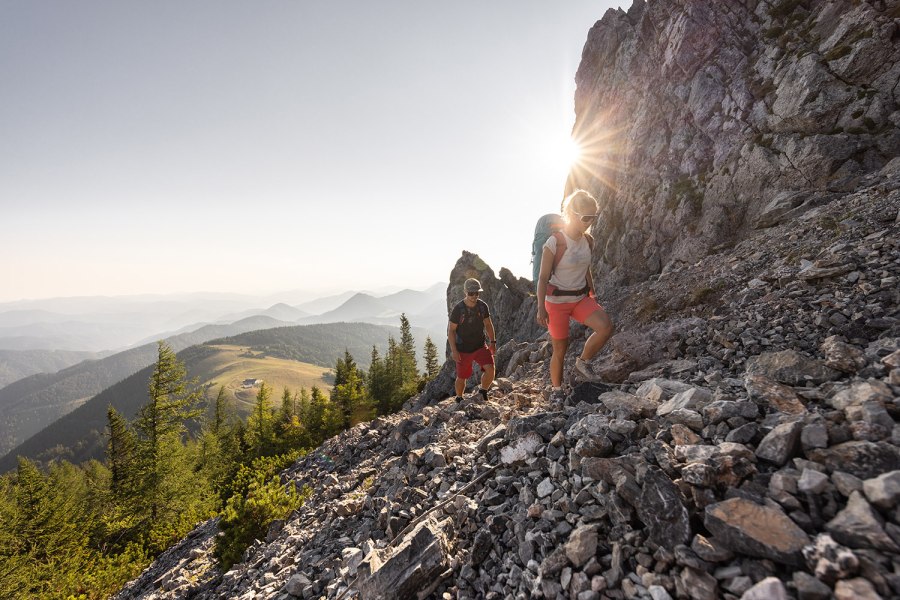 Mann und Frau wandern auf dem Schneeberg. Im Hintergrund die Morgensonne