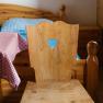 A rustic wooden chair with a heart-shaped cutout in front of a bed at the Edelwei&szlig;h&uuml;tte on Schneeberg