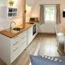 Modern kitchen with wooden floor, white cupboards, dining table and window.