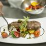 Ein Teller mit kunstvoll angerichtetem Fleisch, Gem&uuml;se und Kr&auml;utern.