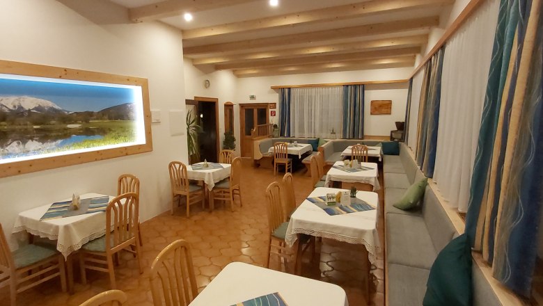 Gem&uuml;tliches Restaurant mit Holzm&ouml;beln und Bergbild an der Wand.