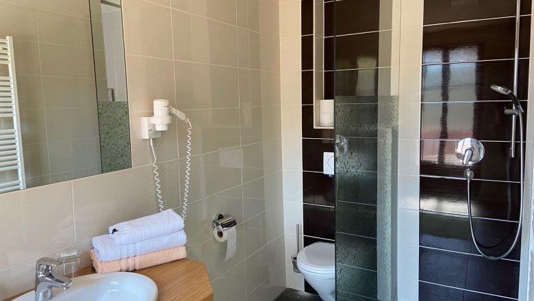 Modernes Badezimmer mit Waschbecken, Spiegel, Handt&uuml;chern, Toilette und Dusche.