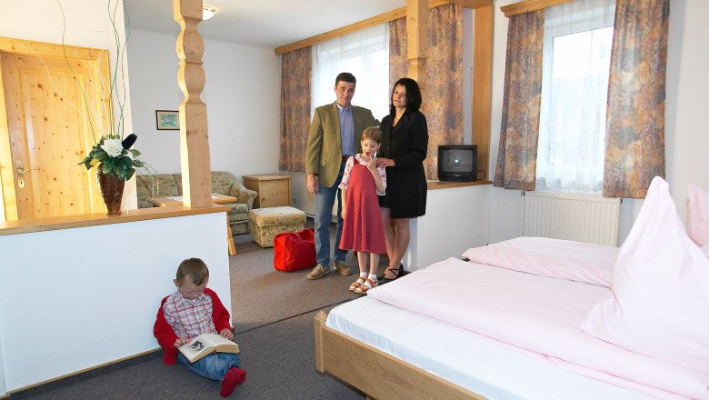 Familie in einem gem&uuml;tlichen Hotelzimmer mit Holzm&ouml;beln und rosa Bettw&auml;sche.