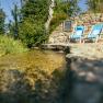 Two blue deckchairs stand next to a small stream in front of a stone wall.