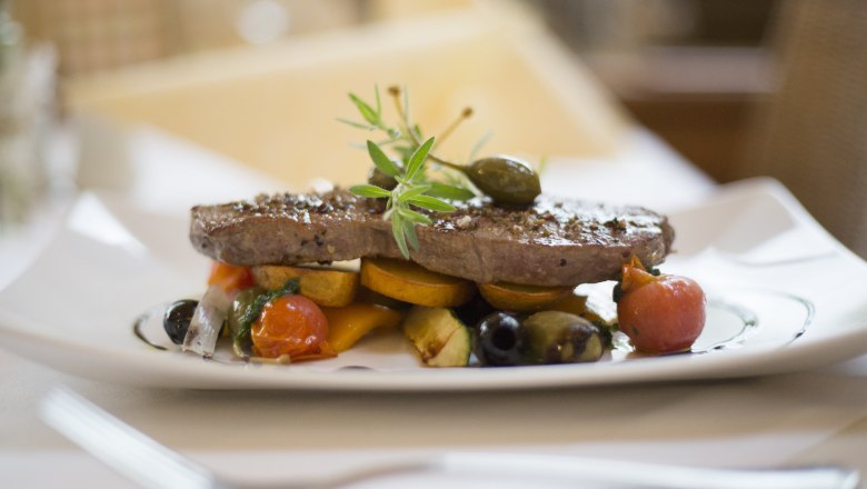 Ein Teller mit einem St&uuml;ck Fleisch, garniert mit Gem&uuml;se und Kr&auml;utern.