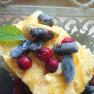 Ein Dessert mit gelbem Eis, roten und blauen Beeren, garniert mit einem gr&uuml;nen Blatt, in einer Glasschale.