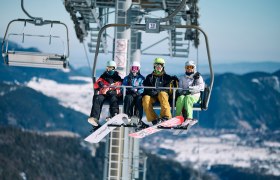 4 Personen sitzen in der Schneeberg Sesselbahn in Wintersportausrüstung