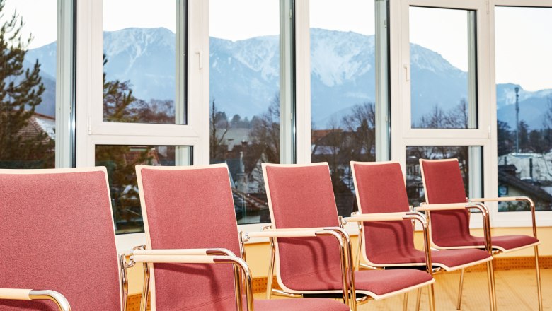 Seminarraum mit roten St&uuml;hlen und Bergblick durch gro&szlig;e Fenster.