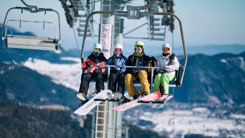 4 Personen sitzen in der Schneeberg Sesselbahn in Wintersportausrüstung