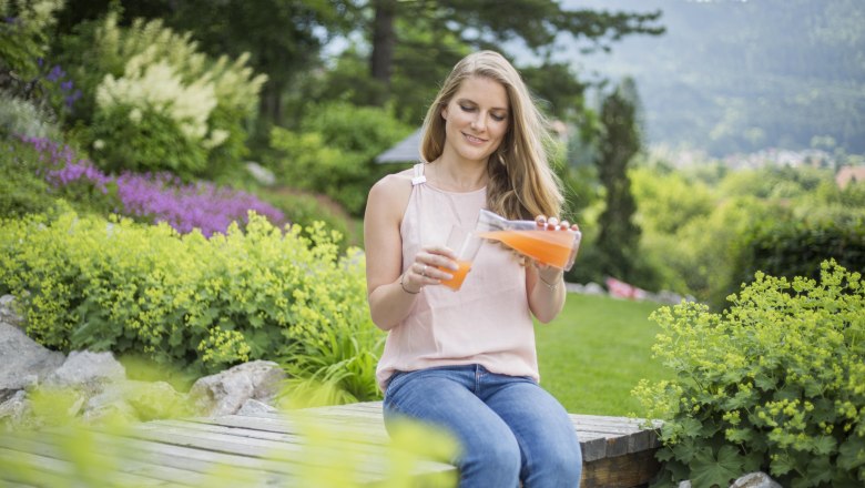 Frau sitzt im Garten und gie&szlig;t Saft in ein Glas.