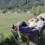 Ein Paar liegt auf einer gro&szlig;en Holzliege in einer gr&uuml;nen Landschaft mit Bergen im Hintergrund.