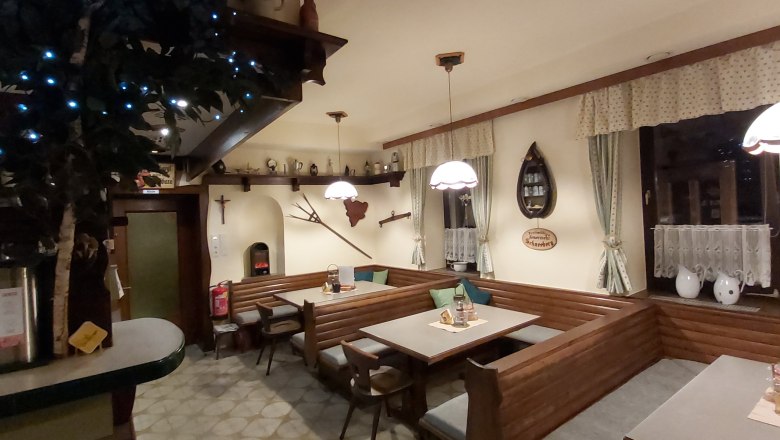 Gem&uuml;tliche Gaststube mit Holzm&ouml;beln, dekorativen Vorh&auml;ngen und rustikalen Accessoires.