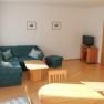 Living room with green corner sofa, wooden table, TV and dining table.